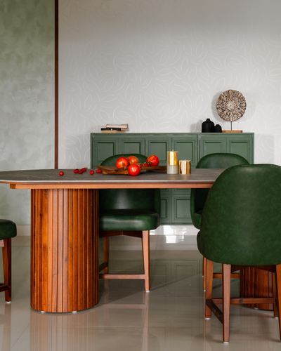 Dining table with fluted wood base and green leather chairs against a green sideboard and textured wall