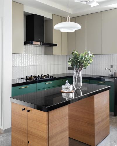 Kitchen with green cabinets, ribbed white tile backsplash, black stone island with wood veneer base and glass vase of eucalyptus