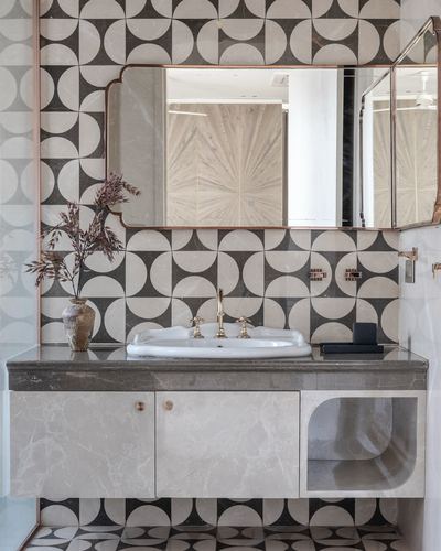 Bathroom vanity with black and white geometric tile, arched pink-framed mirror, and stone counter