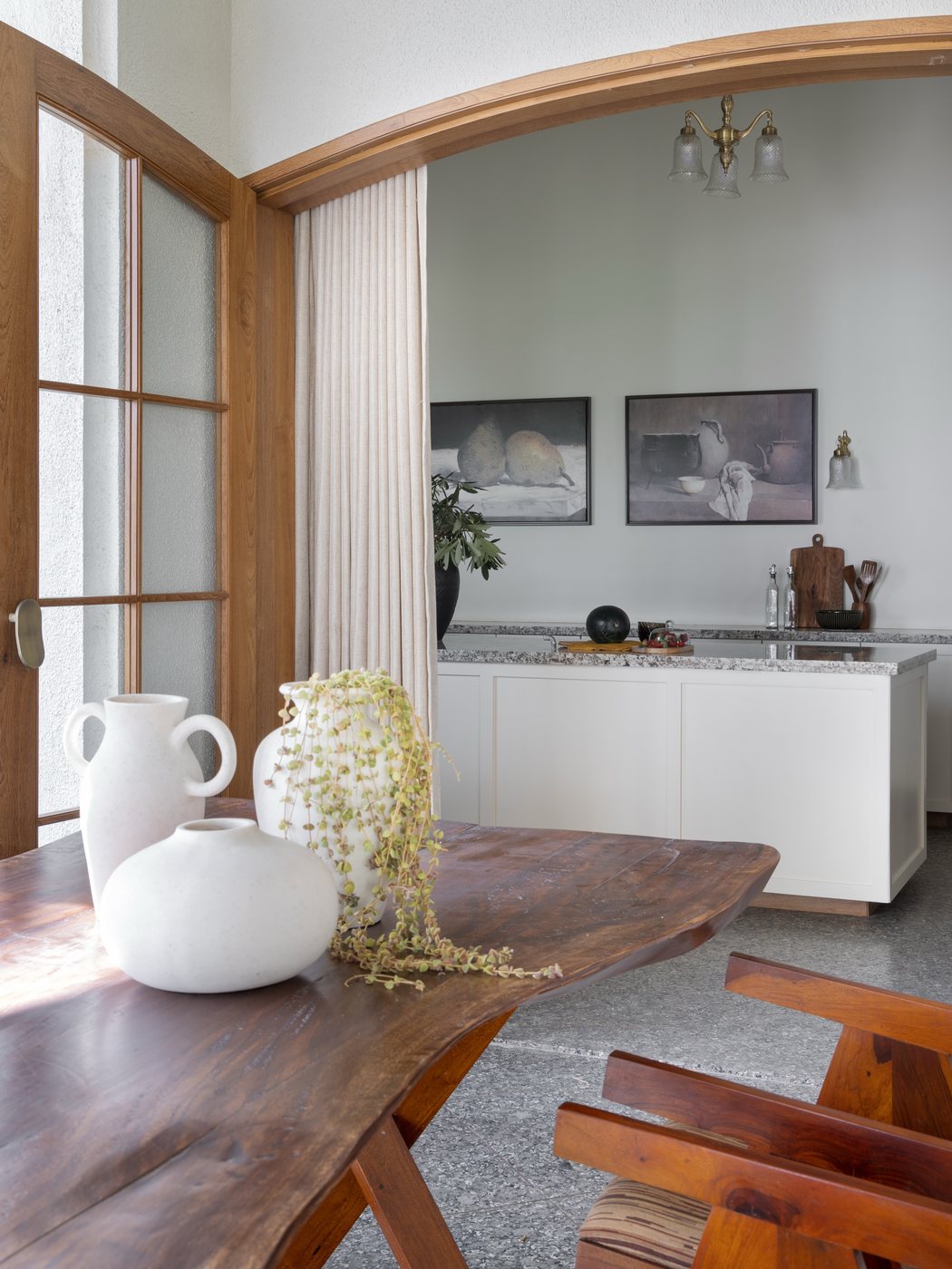 Dining table with ceramic vases under an arched wooden doorway opening to a white kitchen