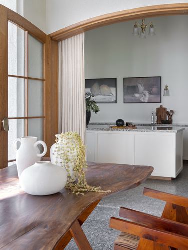 Dining table with ceramic vases under an arched wooden doorway opening to a white kitchen