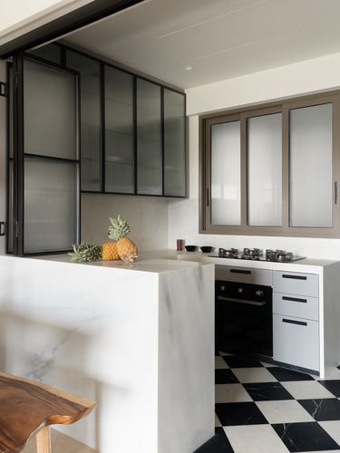 White marble kitchen counter with pineapples, black-white checkerboard floor, reeded glass cabinet doors