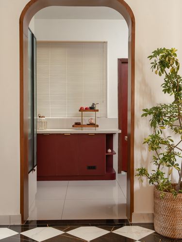 View through an arched wooden doorway into a maroon kitchen counter with blinds behind