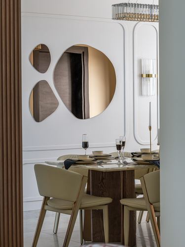 Dining table with cream chairs set before a wall of asymmetric bronze mirrors and paneled molding