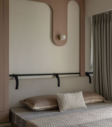 Bedroom headboard wall with rounded pink cut-out, wall sconce, black leather straps, and quilted pillows