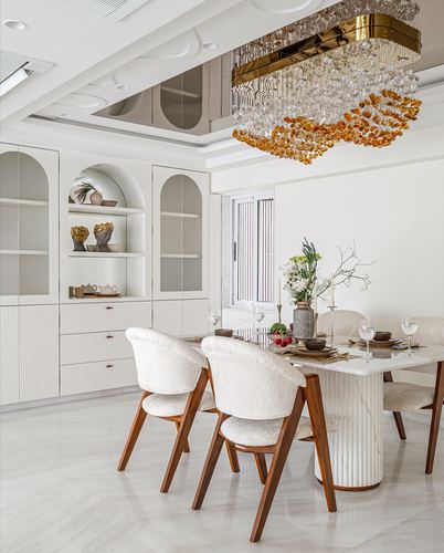 White dining room with fluted marble table, cane-back chairs and amber crystal chandelier
