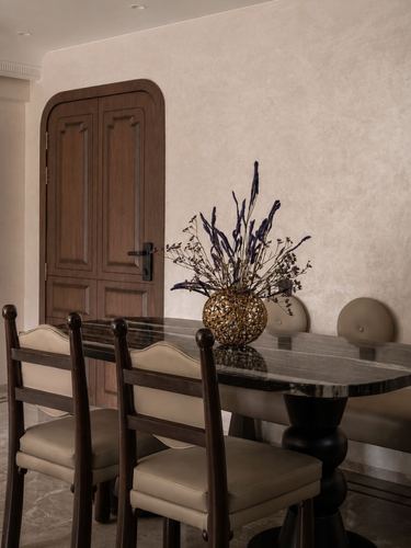 Dining table with dried flower arrangement in front of an arched wooden door and textured plaster wall