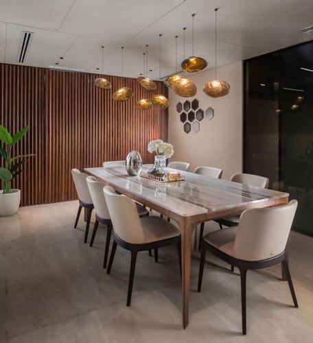 Dining room with marble-topped wood table, cream chairs, wood-slat wall, and cluster of gold pendant lights