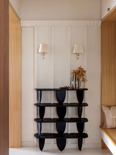Black sculptural console table with paired sconces against paneled wall in wood-framed foyer
