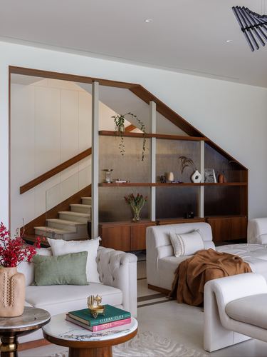Living room with tufted white sofas facing a wood-framed staircase and built-in shelving nook