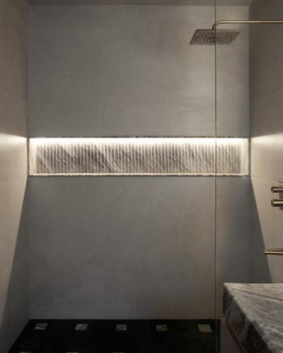 Shower stall with backlit ribbed stone niche and overhead rain shower against grey tiled walls