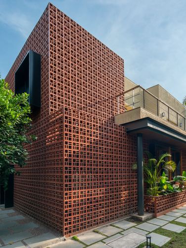 Corner view of a house facade clad in perforated terracotta brick jaali with a black steel column and glass balcony above