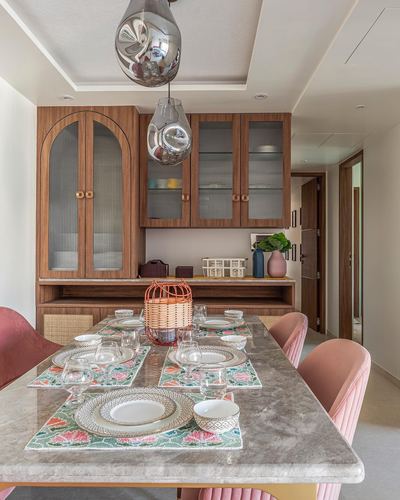 Dining room with marble table set with floral placemats beneath a wooden arched cabinet and glass pendants