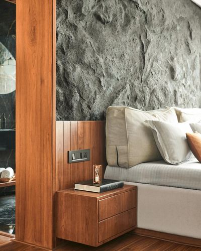 Bedroom corner with textured stone wall, wood-panelled column, and floating wooden nightstand beside bed