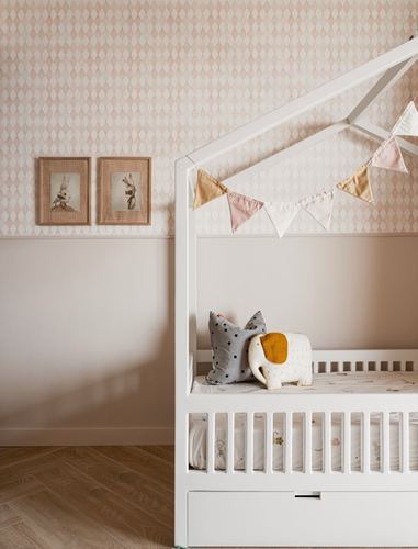 White house-frame crib with pennant bunting in a pink diamond-wallpapered nursery