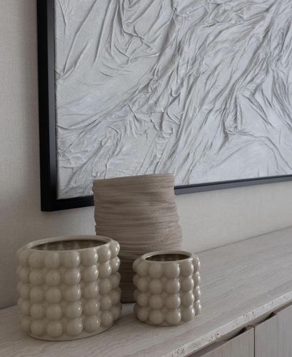 Two bubble-textured ceramic vases and a ribbed vase on a travertine console beneath a textured framed artwork