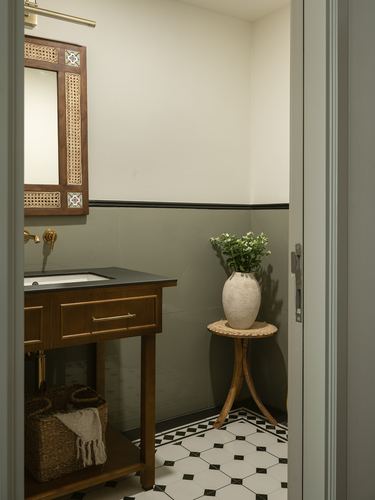 Powder room with wooden vanity, cane mirror, olive walls, and patterned floor tile seen through open door