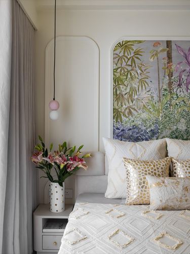 Bedroom corner with arched wall panels, pendant light, and botanical mural headboard behind cream and gold bedding
