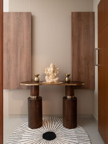 Wooden pooja console with Ganesha idol between fluted cylindrical legs against ribbed wall
