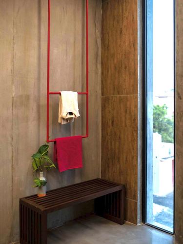 Bathroom corner with red towel ladder, dark wood slatted bench, and stone-clad wall by window