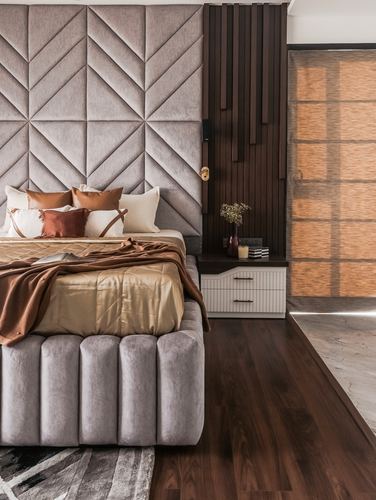 Bedroom with geometric grey headboard, gold and brown bedding, fluted wood accent wall and bedside table