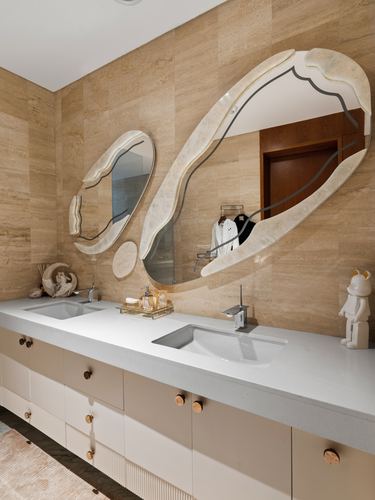 Double vanity bathroom with two organic-shaped mirrors on travertine-look stone wall