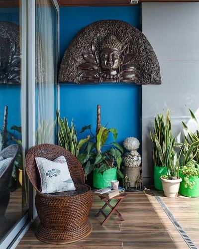 Balcony corner with rattan chair, potted plants, and carved buddha relief on blue wall
