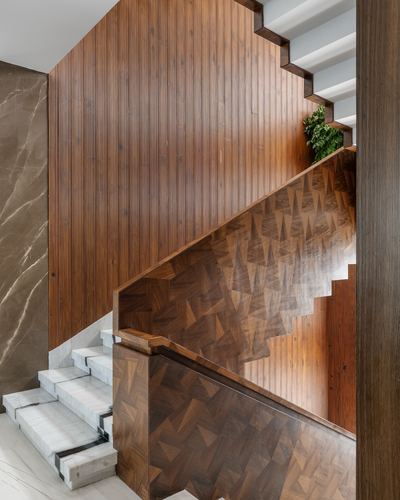 Wooden staircase with end-grain parquet balustrade, fluted wood wall, and marble treads, viewed from below.