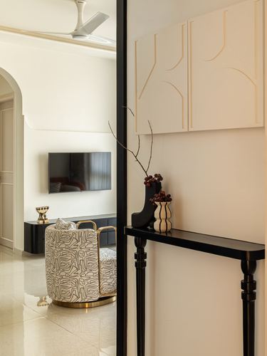 Foyer console table beside carved panel wall, framed view into living room with TV