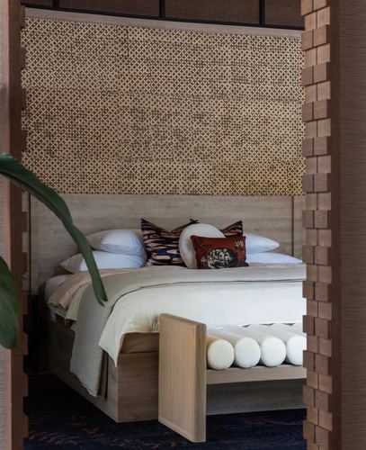 Bed with patterned woven headboard panel viewed through a brick-textured doorway