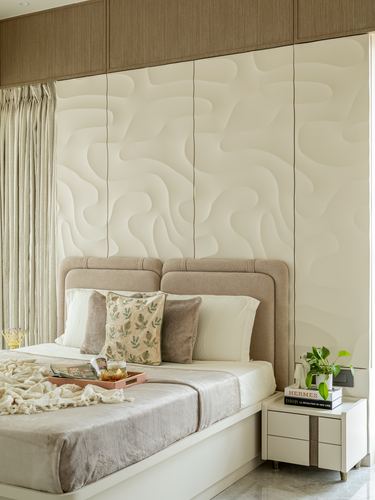 Bedroom with wave-textured cream wall panel behind upholstered double headboard and styled nightstand