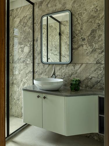 Bathroom vanity with oval vessel sink and black-framed mirror against marbled stone wall