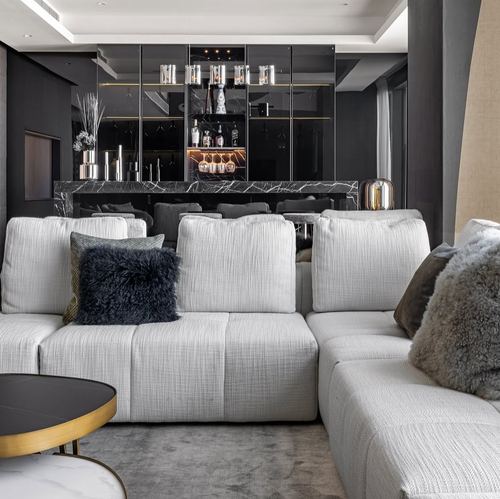 Grey sectional sofa with fur pillows facing a black mirrored home bar with marble counter