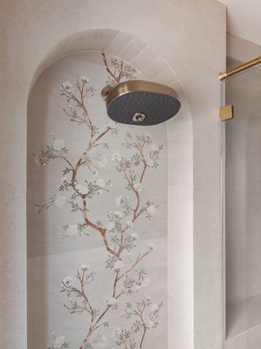 Arched niche with floral wallpaper and brass shower head beside glass shower partition