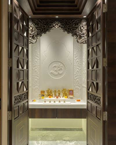 Pooja room niche with carved om motif framed by dark wood lattice doors, Mumbai residence