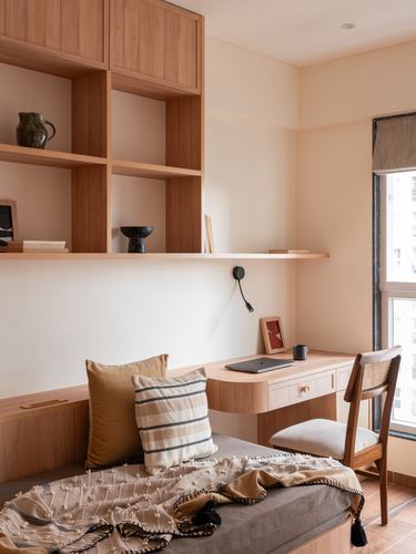 Wooden study nook with open shelving, desk, cane chair and daybed beside a window