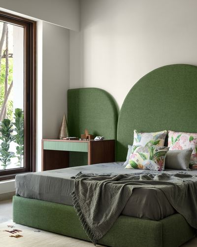 Bedroom with tall arched green upholstered headboard, matching bench, and floor-to-ceiling window