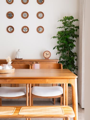 Wooden dining table with cane chairs, decorative wall plates, and a tall potted plant