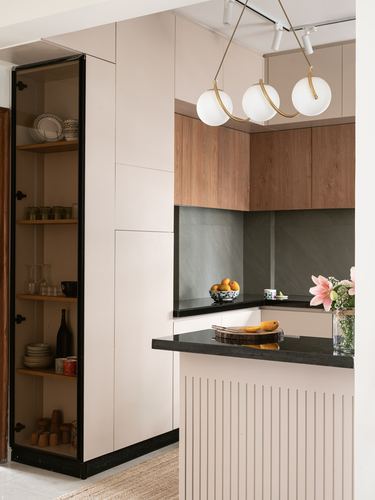 Neutral-toned kitchen corner with wood cabinets, black countertop, and glass display shelf