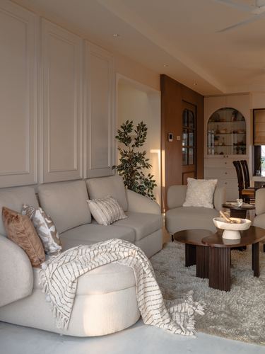 Neutral living room with paneled walls, beige sectional, fluted wood coffee tables and marble bowl in warm light