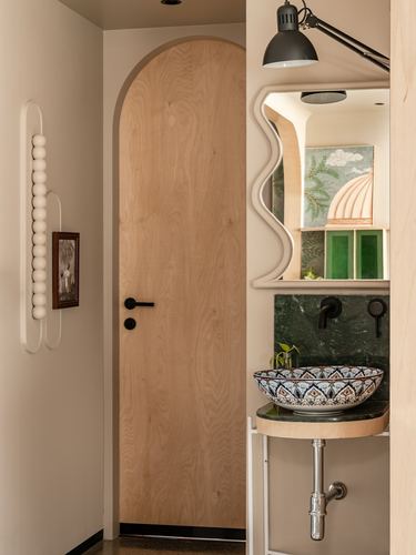Arched wooden door beside a green stone vanity with a patterned ceramic vessel sink and wavy mirror