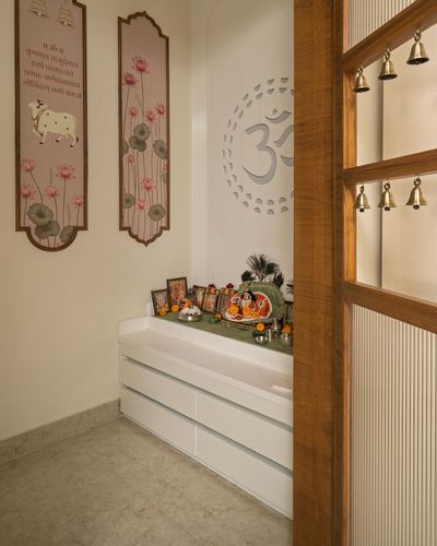 Pooja room niche with white marble console, om wall art, and hanging brass temple bells on wooden door frame