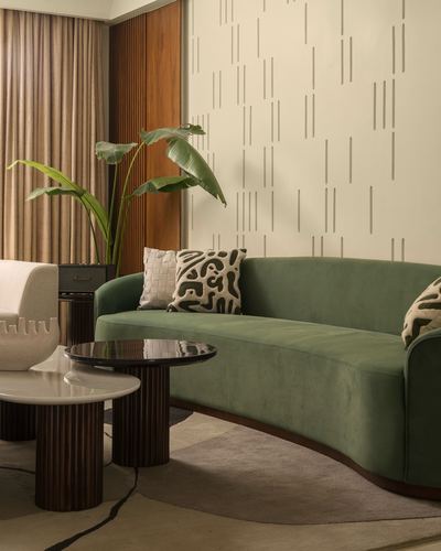Green curved velvet sofa with patterned cushions beside marble and fluted wood side tables in a warm living room
