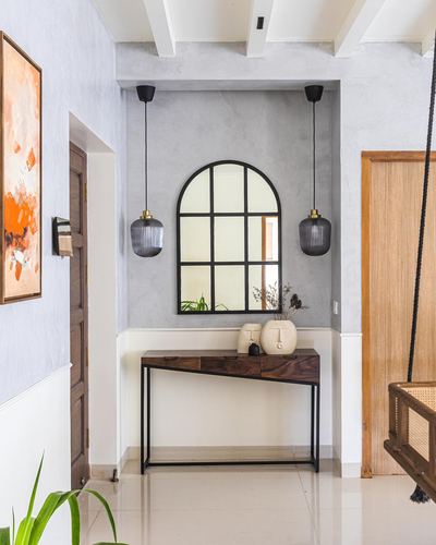 Entryway with arched mirror, twin pendant lights, and wooden console table against grey plaster wall