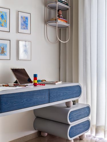 Curved blue-veneer desk with rounded feet beneath framed artwork and a floating shelf
