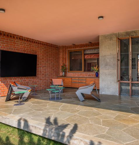 Covered brick terrace with sculptural metal chairs, glass side tables, and stone flooring under a terracotta ceiling
