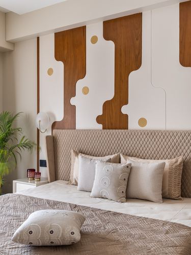 Bedroom with sculptural wood-panel wall, brass dot accents, quilted headboard and layered cushions