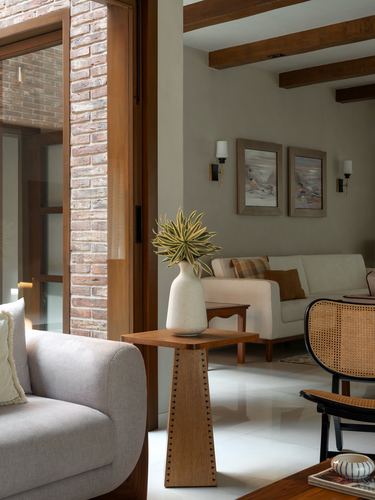 Living room corner with exposed beams, brick doorway, cane chair, and wooden side table holding a vase