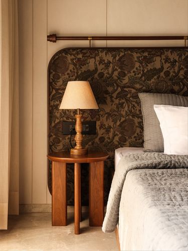 Bedside vignette with carved wood table, turned lamp, and arched floral upholstered headboard