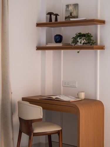 Wooden curved desk with chair beneath floating wood shelves styled with plants and books